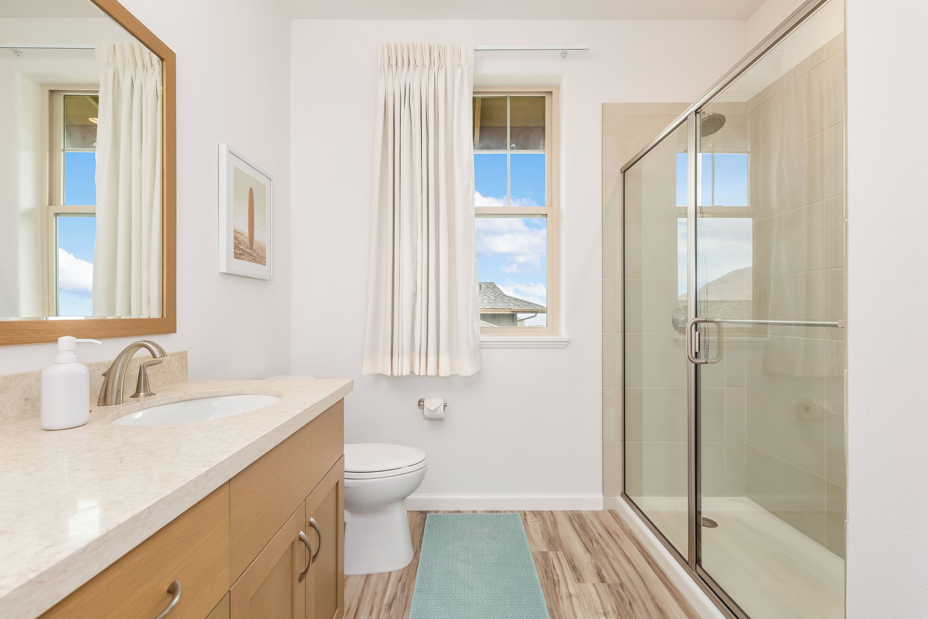 A bathroom with a glass shower, a sink, a toilet, and a window with curtains.