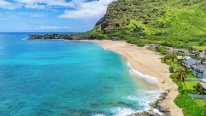 Un complejo turístico frente al mar con playa, océano y montañas al fondo.