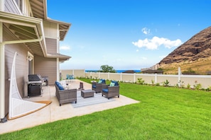 A backyard with outdoor furniture, a grill, and a view of the ocean. - Ocean View Exquisite Home at Cottages at Mauna Olu Near Beach W/outdoor Games (Waianae)