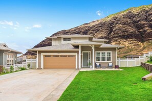 Ein zweistöckiges Haus mit Garage, einer Veranda mit Sitzgelegenheit und einem Berg im Hintergrund.