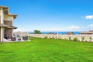 A residential backyard with a lawn, outdoor furniture, and a white fence. - Ocean View Exquisite Home at Cottages at Mauna Olu Near Beach W/outdoor Games (Waianae)