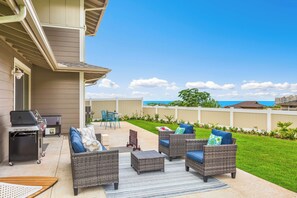 Eine Terrasse im Freien mit Korbmöbeln, einem Grill und Blick aufs Meer.