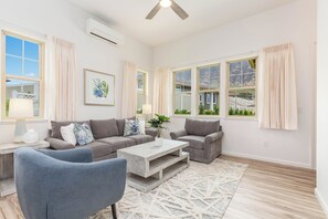 Ein geräumiges Wohnzimmer mit grauem Sofasatz, einem Couchtisch und einem Deckenventilator.