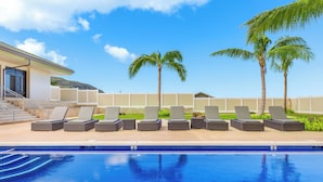 Un área de piscina con sillones de descanso y palmeras.