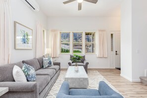 Ein geräumiges Wohnzimmer mit grauem Sofa, Couchtisch und Blick auf eine Berglandschaft durch große Fenster.