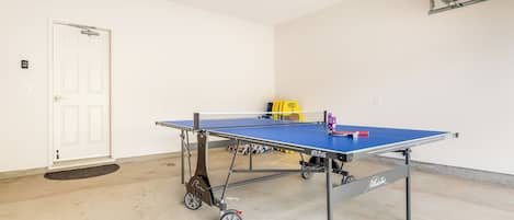 Una mesa de ping pong en una habitación con una puerta blanca, un interruptor de luz y una lámpara en el techo.