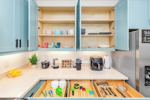 A modern kitchen with open cabinets, a countertop with various appliances, and a drawer organizer. - Ocean Views Serene Vacation Escape Home Near Beach W/beach Equipment & Games (Waianae)