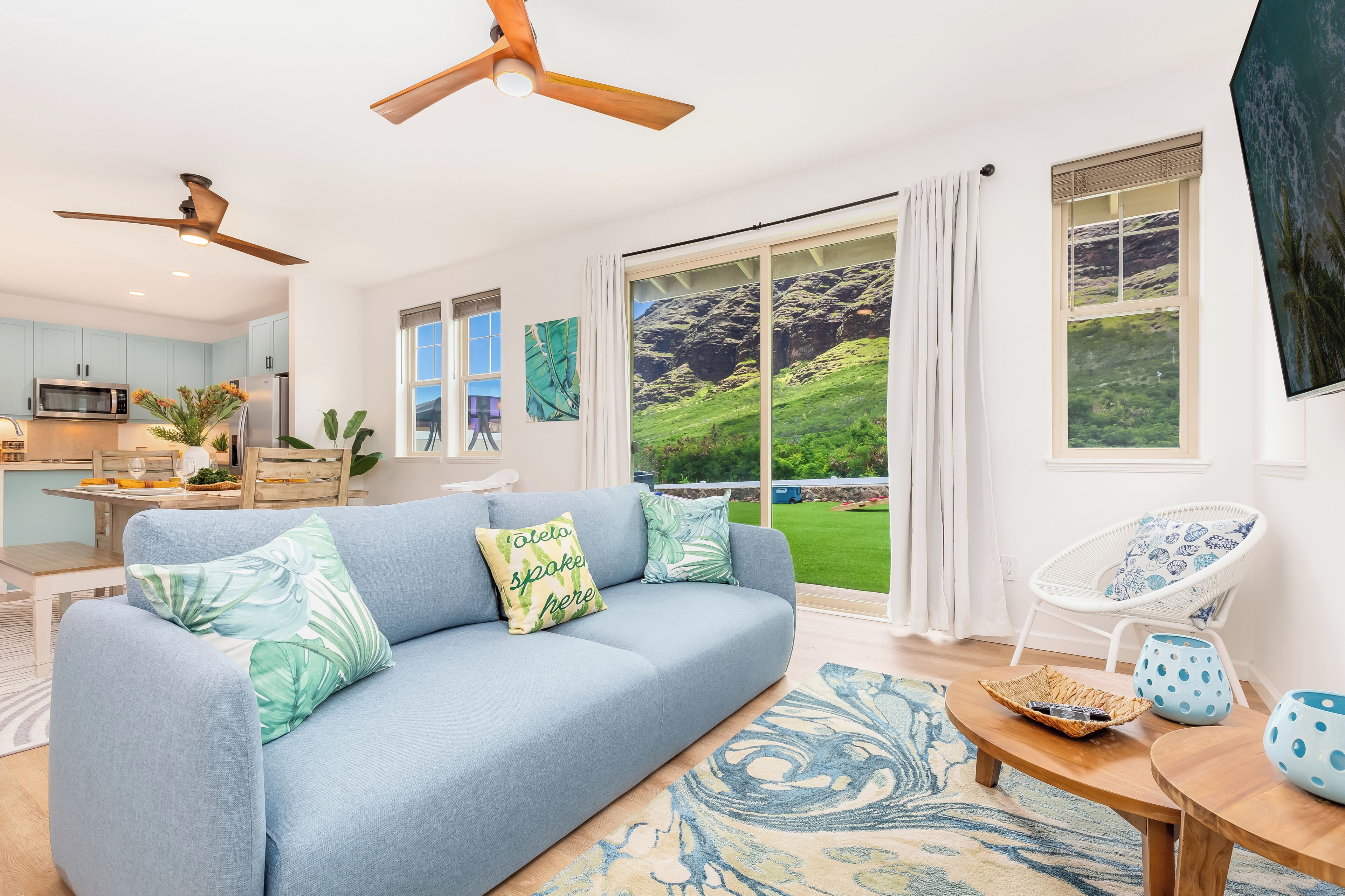 A modern living room with a blue sofa, a dining area with a wooden table, and a kitchen with a microwave.