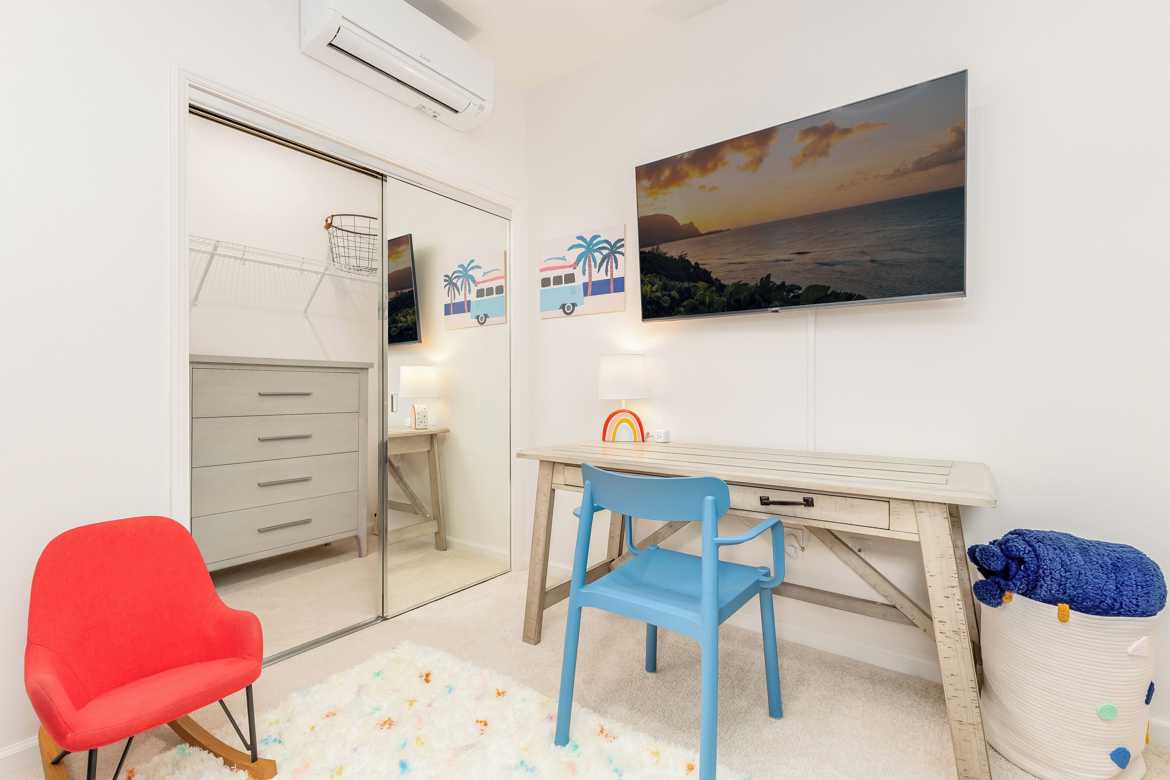 Une pièce comprenant un bureau, une chaise et un fauteuil rouge. Un mur blanc est décoré d’un tableau, et il y a aussi un climatiseur.
