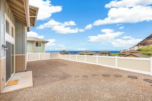 Ein Wohnhaus mit Kiesterrasse, weißem Zaun und Blick auf das Meer.