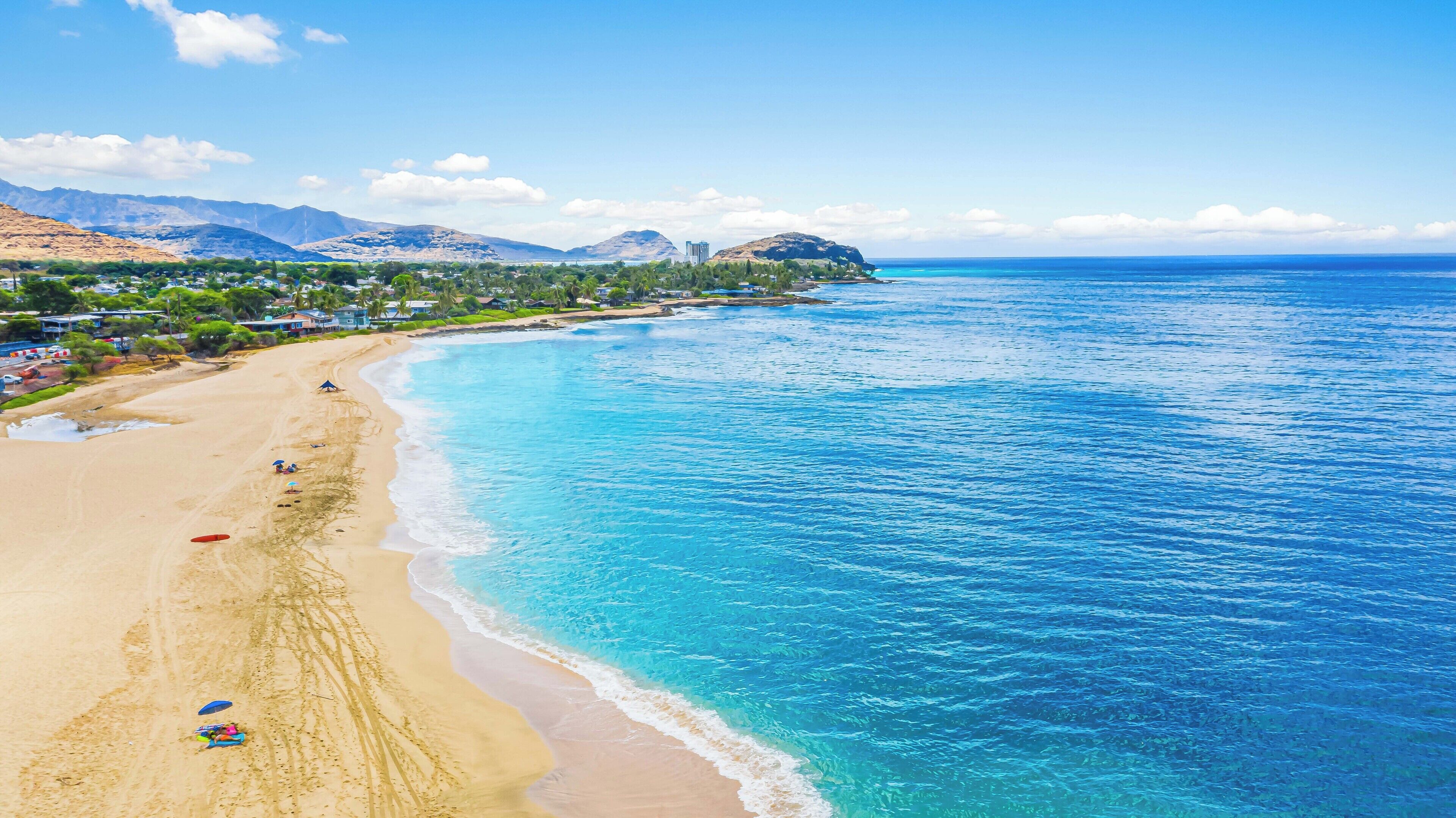 Una playa costera con aguas azules cristalinas, una orilla arenosa y montañas al fondo.