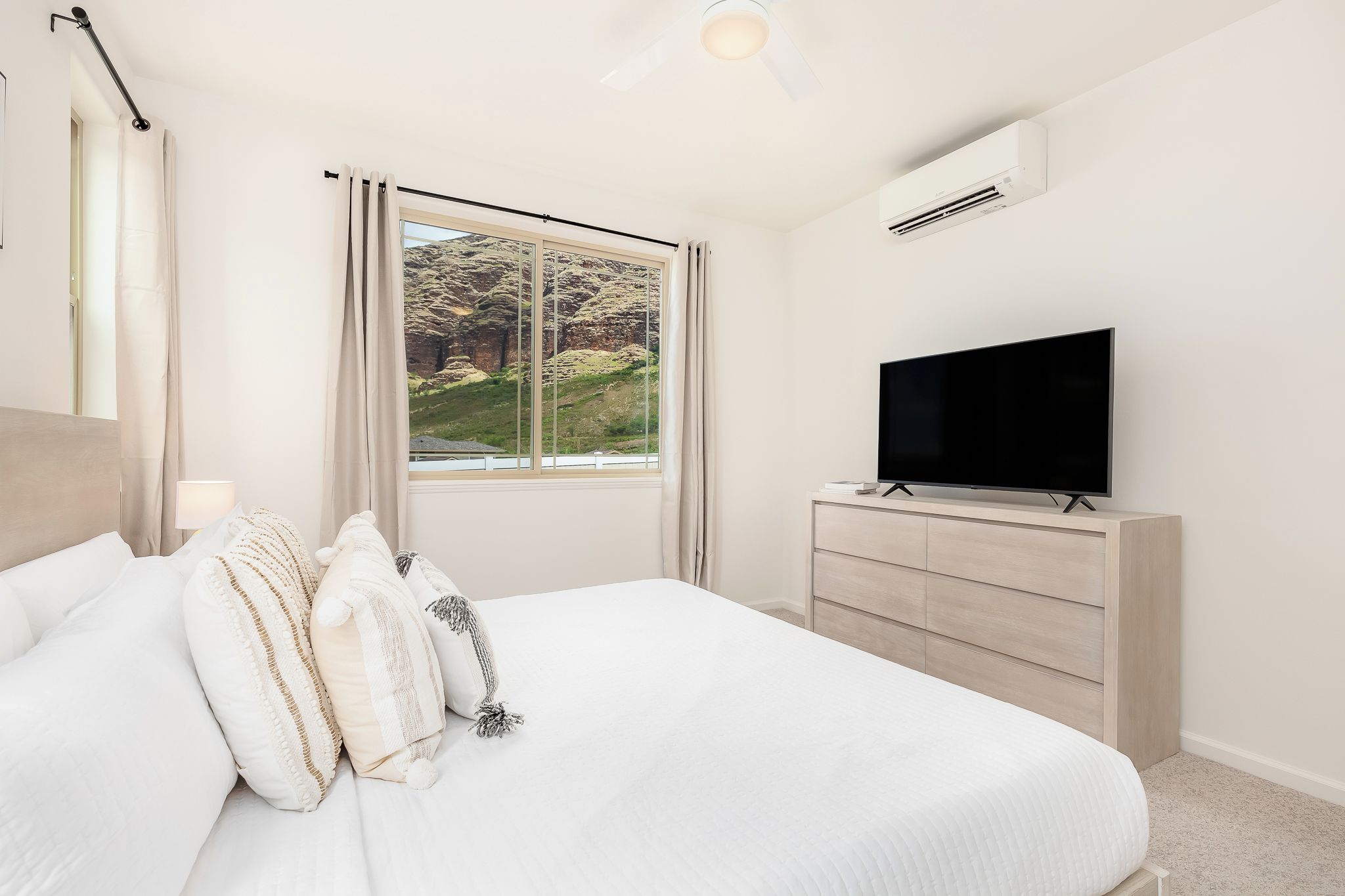 Ein Schlafzimmer mit einem Bett, einem Fernseher, einer Kommode und einem Fenster mit Blick auf eine Berglandschaft.