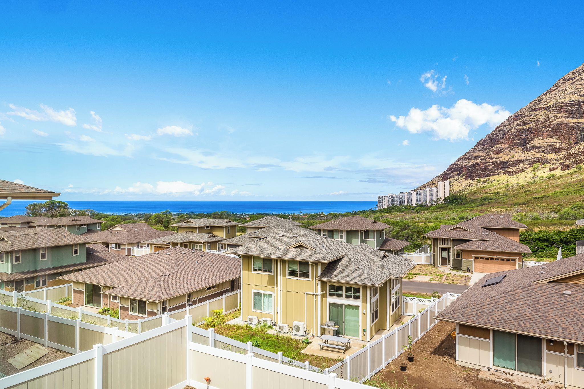 A residential area with multiple houses, a clear view of the ocean, and a mountain in the background.