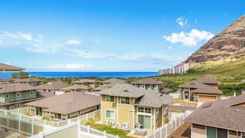 A residential area with multiple houses, a clear view of the ocean, and a mountain in the background.