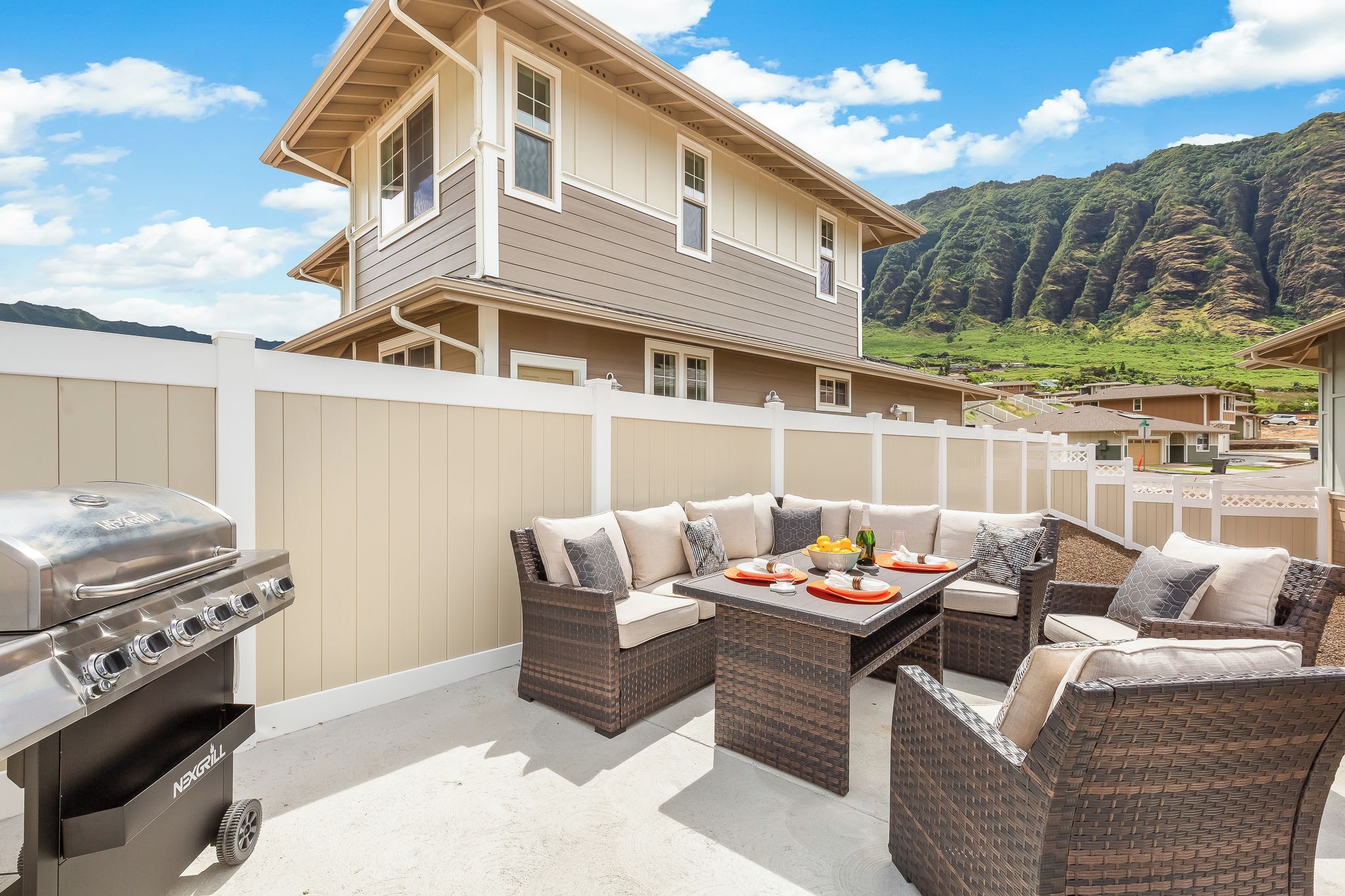 A patio with outdoor furniture, a grill, and a view of a house and mountains.