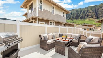 A patio with outdoor furniture, a grill, and a view of a house and mountains.