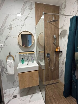 A modern bathroom with a glass-enclosed shower, a wooden vanity, a round mirror, and a towel rack. - Peaceful 1-bedroom apartment with AC in charming Podgorica (Podgorica)