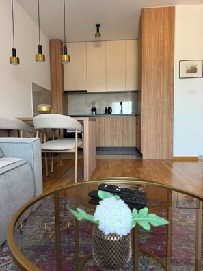 Un salon moderne avec un canapé, une table basse agrémentée d’un vase, et un coin cuisine doté de meubles en bois et d’un plan de travail.