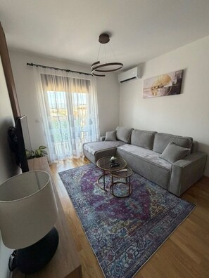 Un salon moderne avec un canapé gris, un tapis à motifs, une table basse ronde et un luminaire suspendu au plafond.