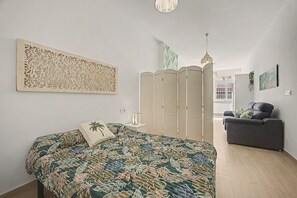 Ein Schlafzimmer mit einem Bett, einem Nachttisch, einem dekorativen Raumteiler, einem Sofa und Blick ins Freie.
