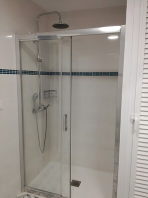 Een douchecabine met glazen wanden, een handdouche en een handmixer.