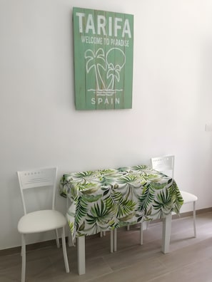Een eethoek met een tafel bedekt met een tafelkleed met een bladmotief, twee witte stoelen en een bord met de tekst 'TARIFA WELCOME TO PARADISE SPAIN'.