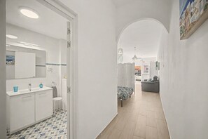 Ein Flur mit einem Badezimmer links, einem Bett in der Mitte und einem Sofa rechts.