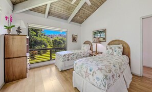 Ein Schlafzimmer mit zwei Betten, einer Holzbalkendecke, einem großen Fenster mit Blick auf Grünflächen und einem kleinen Tisch mit Lampe.