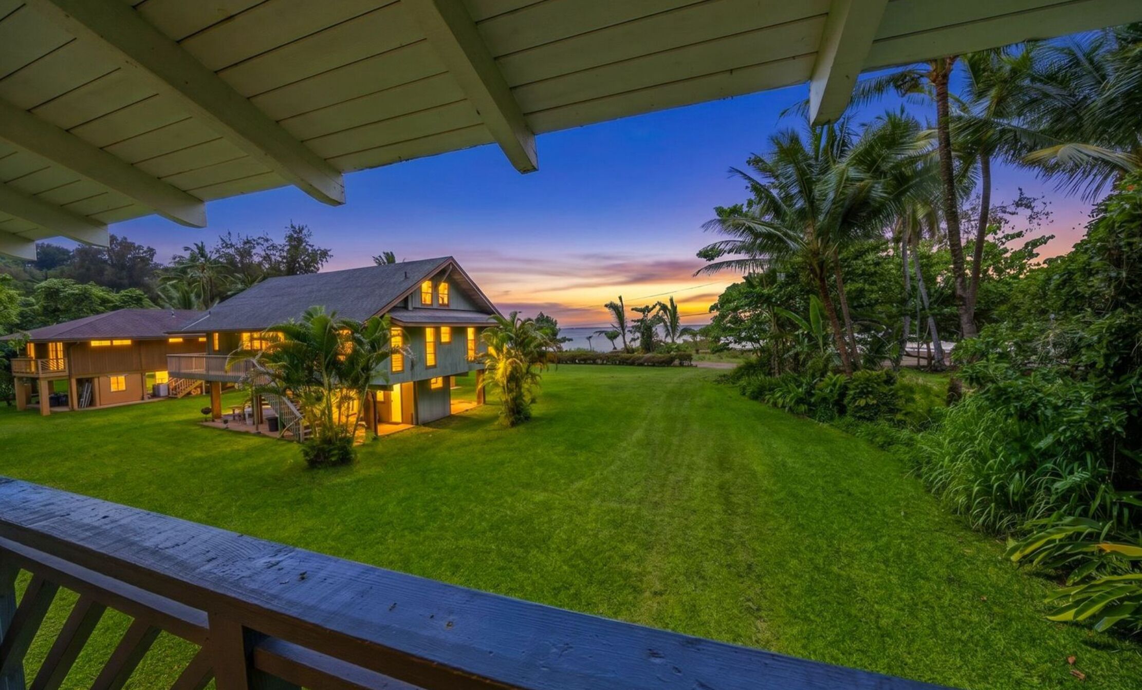 A two-story house with a well-maintained lawn and a view of the ocean at sunset.