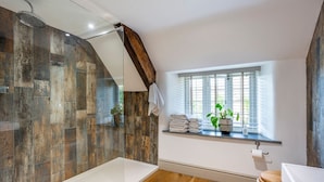Ein Badezimmer mit Dusche, Holzboden, einem Fenster mit Pflanzen und einer Toilette.
