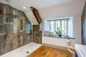 Een badkamer met een douche, houten vloer, een raam met planten en een toilet.