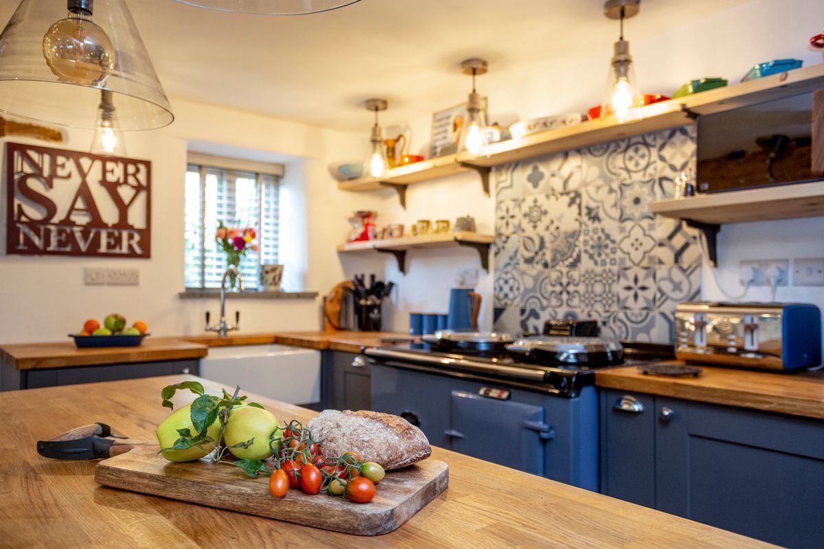 A kitchen with a wooden countertop, a cutting board with apples and tomatoes, a bread loaf, and a hanging light fixture.