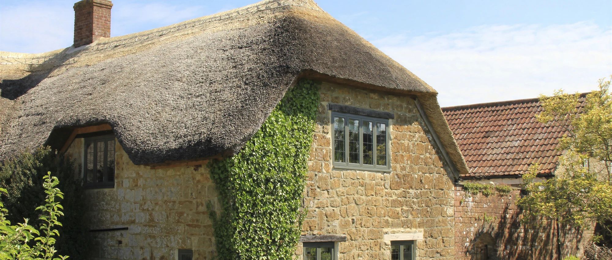 A traditional stone cottage with a thatched roof, ivy-covered walls, and a window.