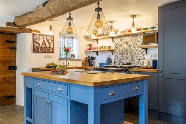 A kitchen with a blue island, hanging pendant lights, and a 'NEVER SAY NEVER' sign.