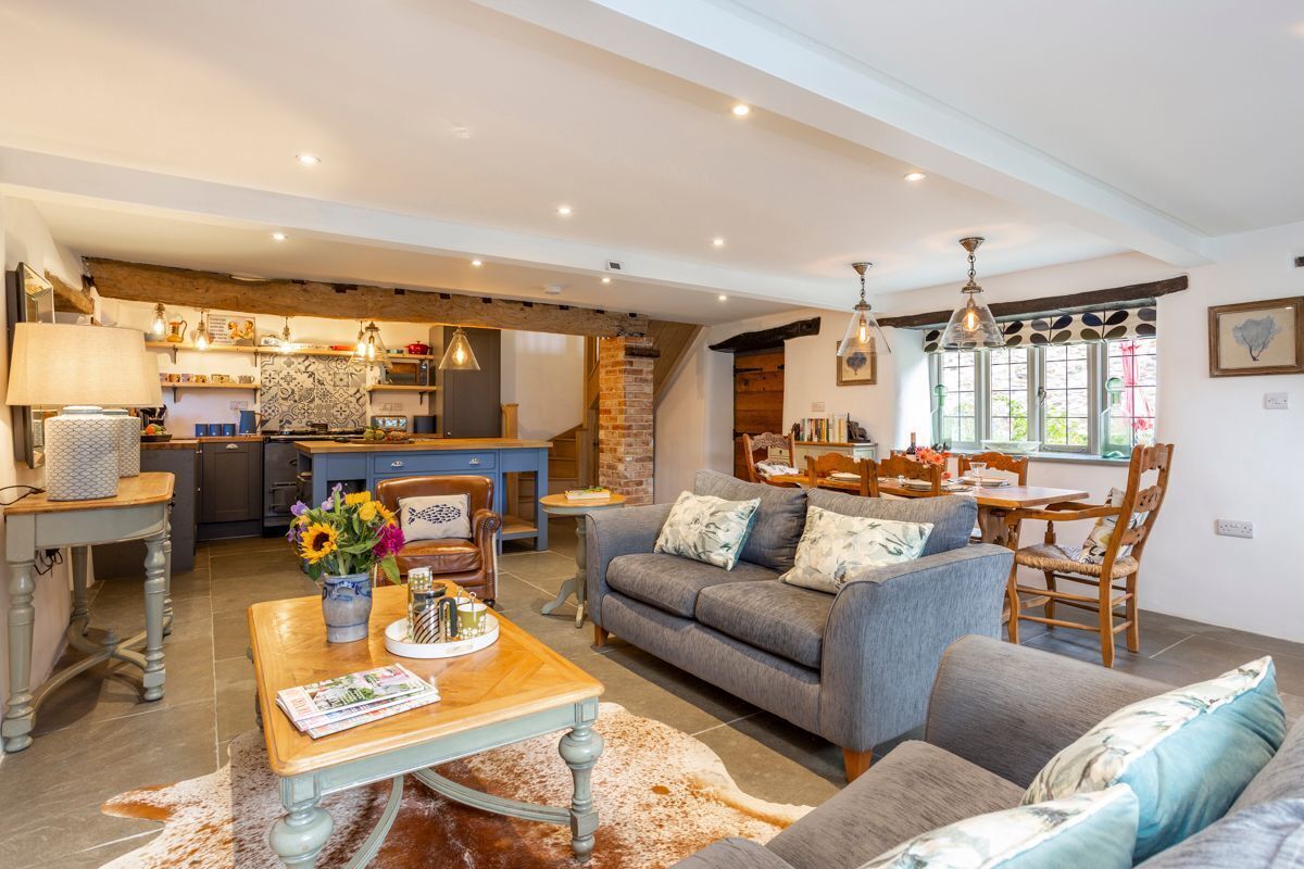 A spacious living area with a sofa, coffee table, and dining table. There is a kitchen in the background with a brick wall and pendant lights.