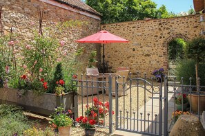 A stone wall, a metal gate, and a red umbrella in a garden.