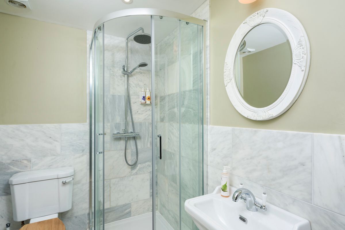 Un baño con ducha envuelta en vidrio, inodoro, lavamanos con espejo y pared con azulejos de mármol.