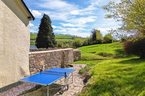Ein Tischtennis-Tisch steht auf einer Steinterrasse mit Blick auf eine grüne Landschaft und ein Gebäude im Hintergrund.
