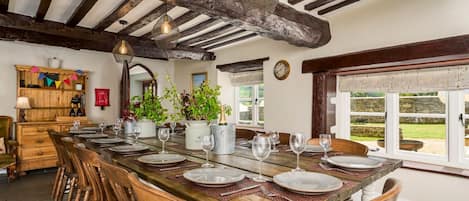 A dining area with a long wooden table set for six, surrounded by wooden chairs.