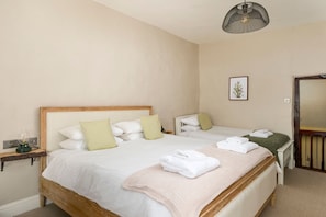 Un lit double avec une tête de lit en bois, deux tables de chevet, une lampe fixée au mur et un tableau encadré.