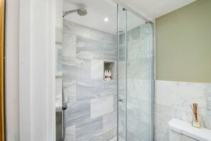 Un bagno moderno con doccia vetro, piastrelle in marmo e water con dispenser di sapone.