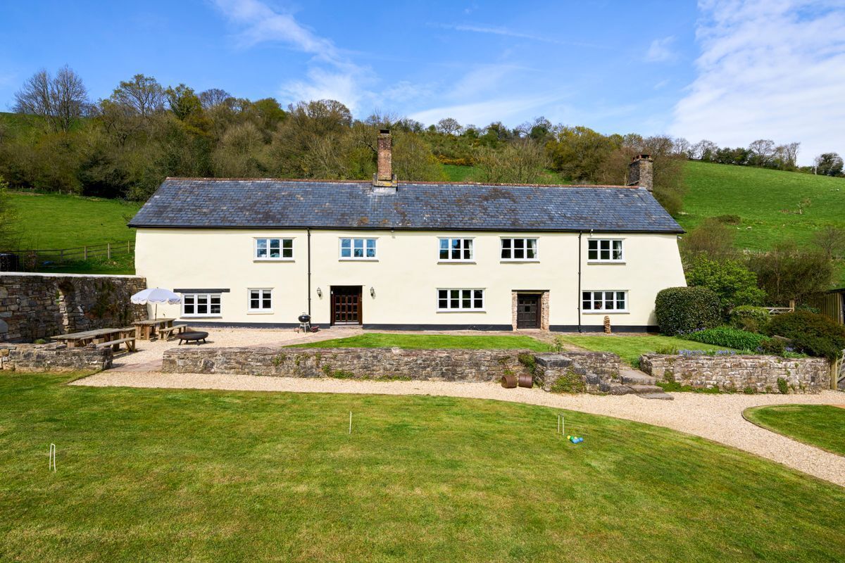 A two-story house with a stone foundation, a grassy yard, and a paved driveway.