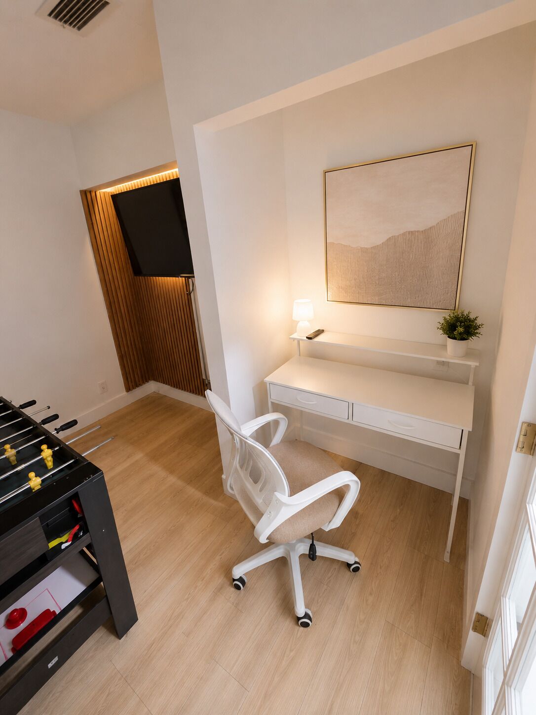 A modern room with a foosball table, a desk with a lamp, and a mounted TV.