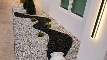 Un bâtiment moderne avec un chemin menant à l’entrée, entouré de petits galets blancs et agrémenté d’un motif en gravier noir.
