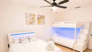 A bedroom with a large bed, a bunk bed, a ceiling fan, and artwork on the wall. - Elegant 4BR Retreat Near Tampa with Private Office (Brandon)