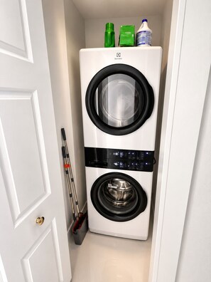 A compact, white wall-mounted washer and dryer unit with a control panel and a small storage area above.