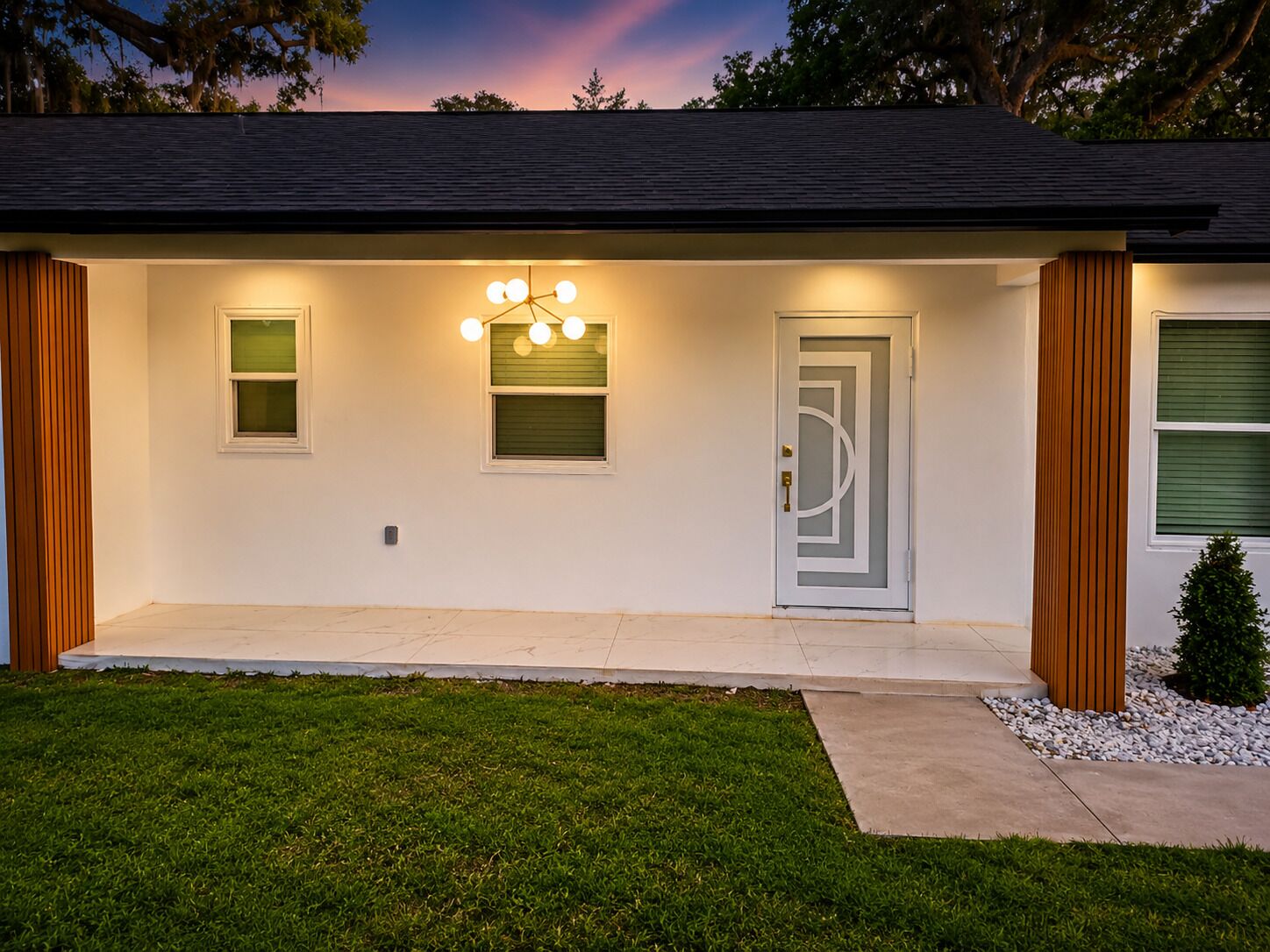 Une maison moderne dotée d’un porche à l’avant, d’une porte au motif géométrique et d’un luminaire placé au-dessus de la porte.