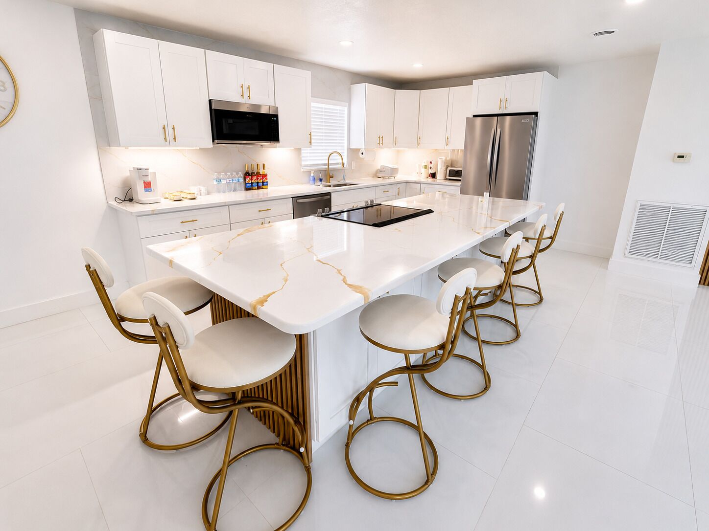 A modern kitchen with white cabinetry, a large island with bar stools, stainless steel appliances, and a marble countertop.
