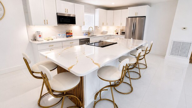 A modern kitchen with white cabinetry, a large island with bar stools, stainless steel appliances, and a marble countertop. - Elegant 4BR Retreat Near Tampa with Private Office (Brandon)