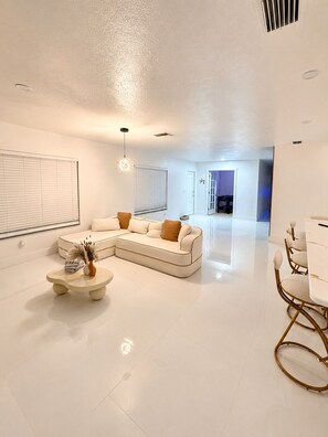 A modern living room with a sectional sofa, a coffee table, and a dining area with chairs.